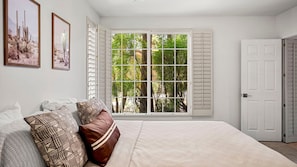 A bedroom with a large bed, a window with shutters, and two framed pictures on the wall. - Roadrunner Haven — warm and welcoming Monthly Rent (Scottsdale)