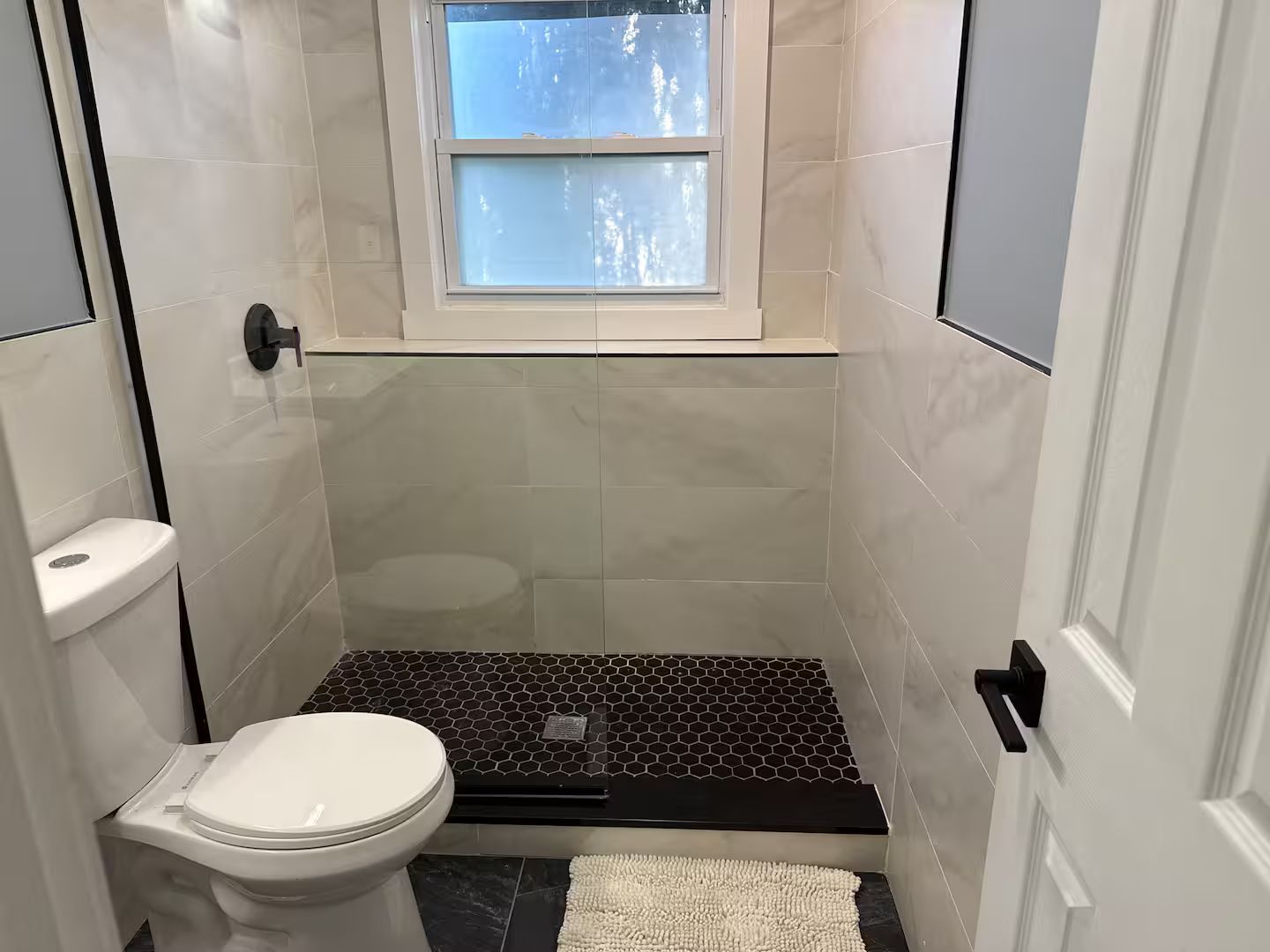 A small, modern bathroom with a toilet, a shower area, and a window.