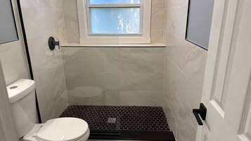 A small, modern bathroom with a toilet, a shower area, and a window.