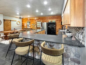 A modern kitchen with a central island, bar stools, and a stone accent wall. - Graceland - Dogs OK | Hot Tub | Game Room | EV Charger (Blue Ridge)