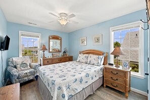 Un dormitorio con cama, una silla, cómoda, ventilador de techo y ventana con vista.