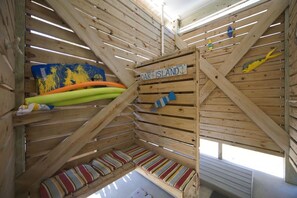 Interior de una cabaña de madera con techo inclinado, un cartel que dice 'Oak Island' y cojines con rayas de colores en la zona de estar.