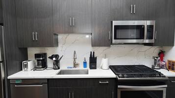 A modern kitchen with dark wood cabinets, a stainless steel microwave, a coffee maker, and a gas stove.