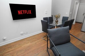A modern living room with a flat-screen TV mounted on the wall displaying 'NETFLIX'.