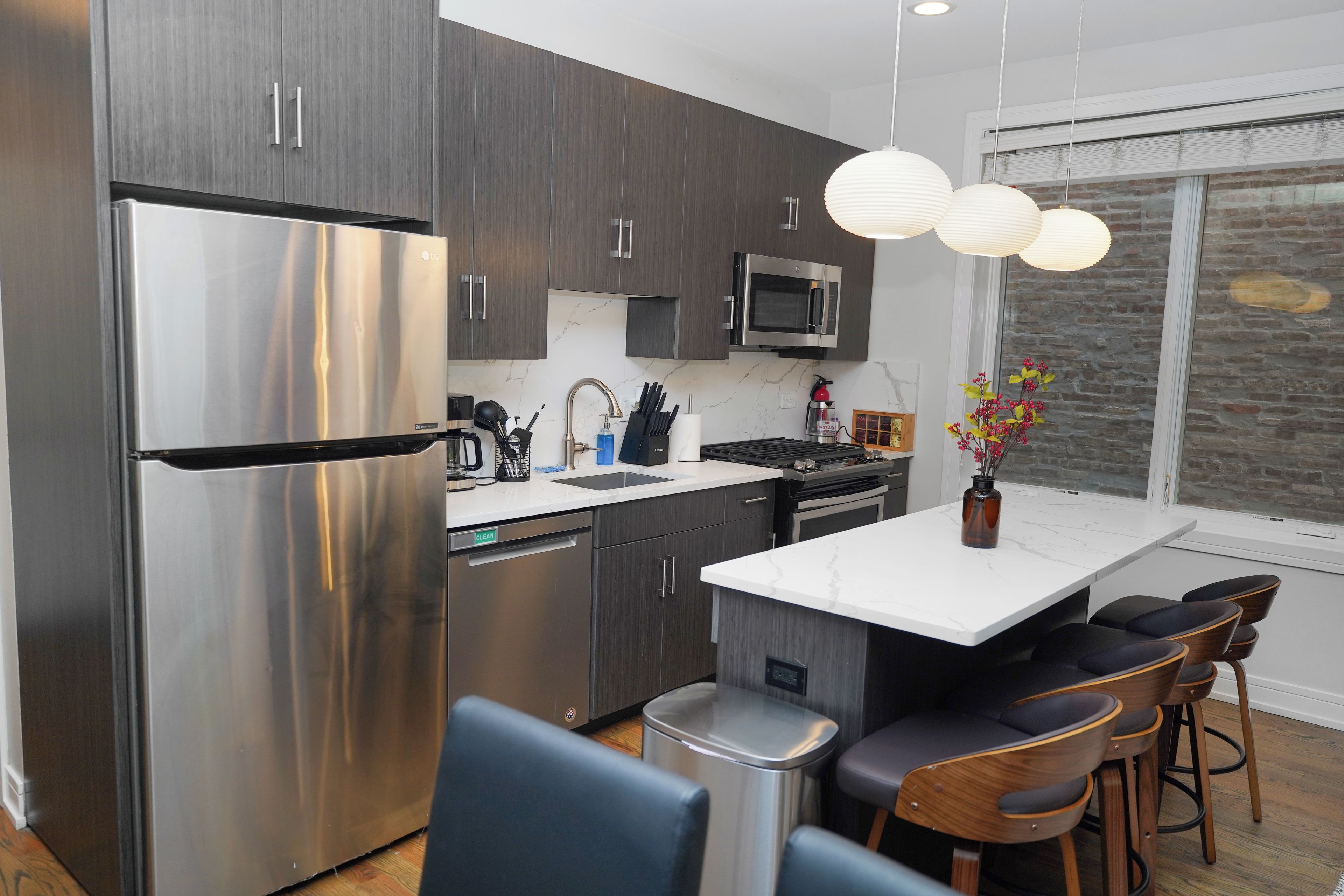 A modern kitchen with stainless steel appliances, a central island with bar stools, and a hanging light fixture.