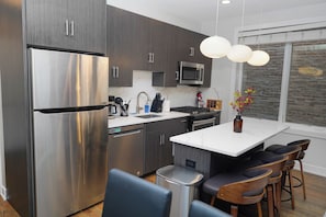 A modern kitchen with stainless steel appliances, a central island with bar stools, and a hanging light fixture.