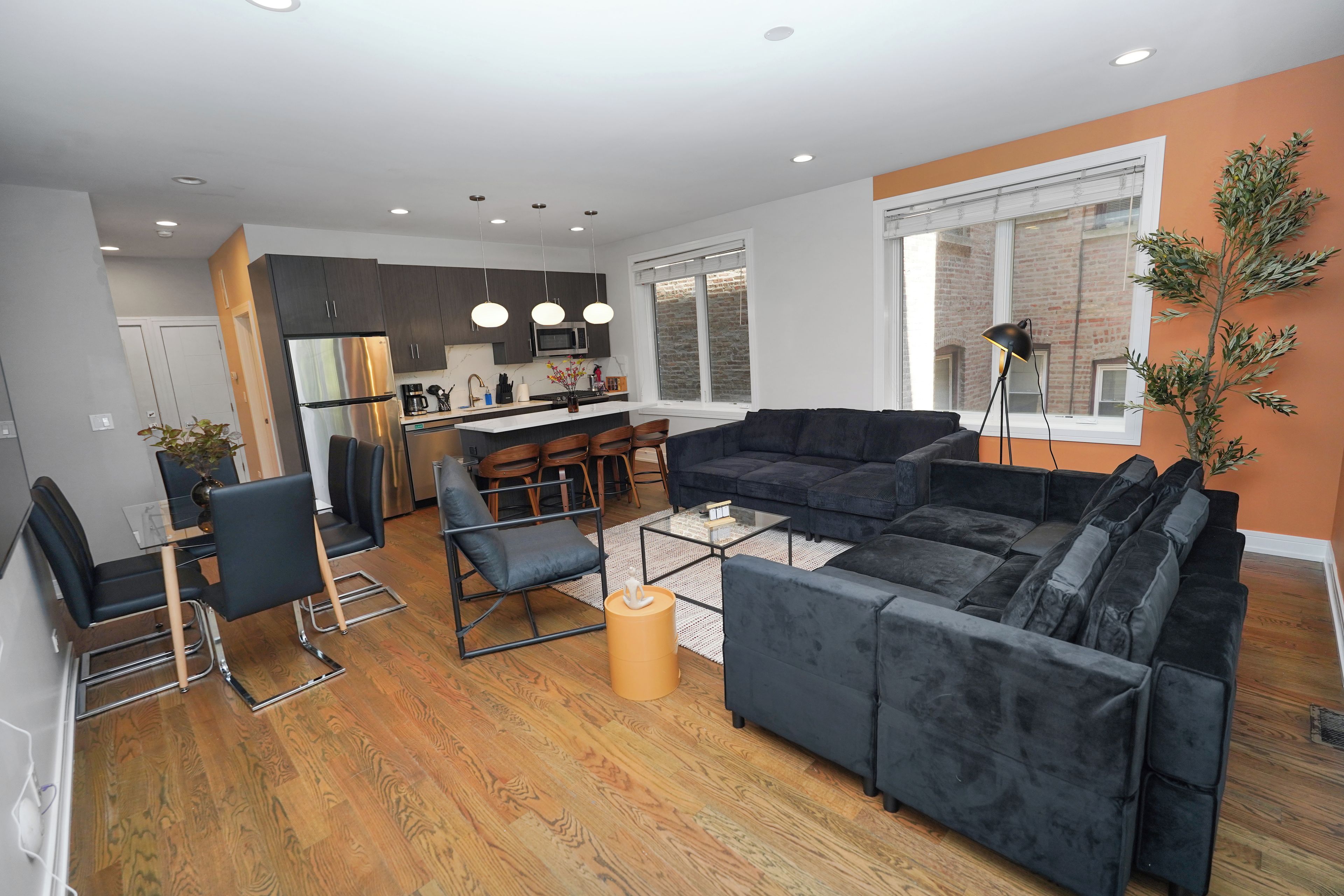 A modern living room with a sectional sofa, a coffee table, and a dining area with chairs and a kitchen in the background.
