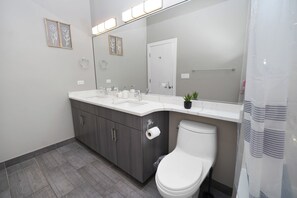 Un baño moderno con inodoro blanco, tocador con espejo y cortina de ducha.