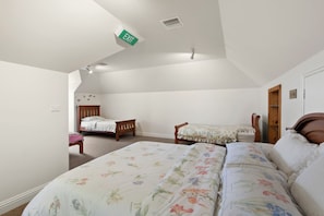 A bedroom with a large bed, two smaller beds, a wooden bench, and an exit sign on the ceiling.