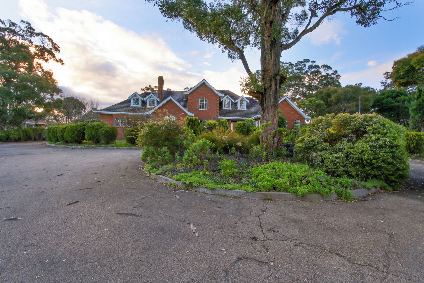 A two-story house with a brick exterior, a chimney, and a driveway leading to a parking area.