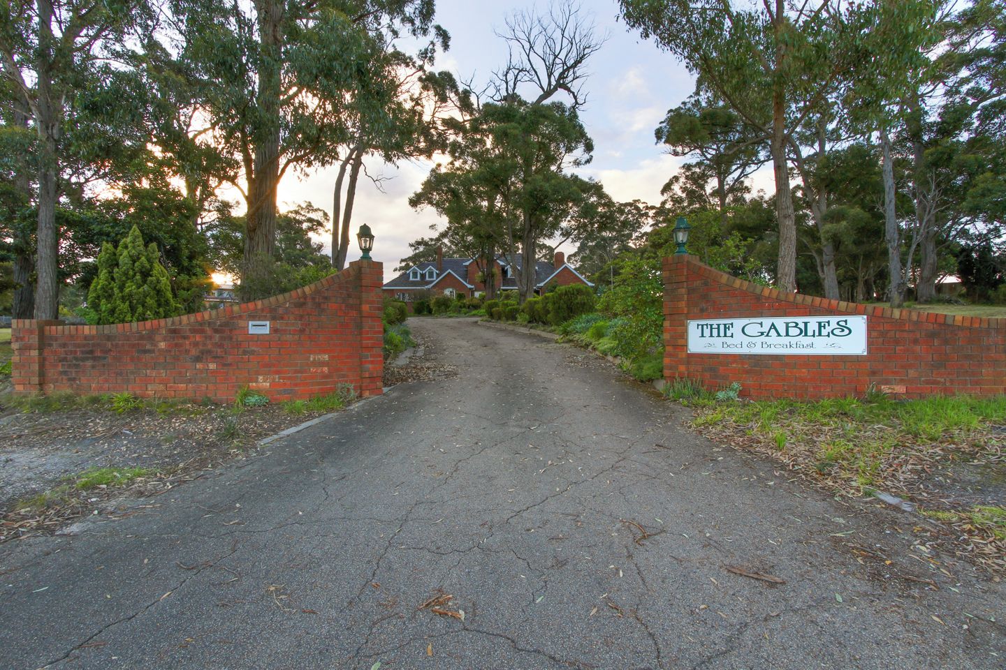 Una entrada protegida por un portón a una propiedad llamada 'The Cables', con un muro de ladrillo y un cartel.