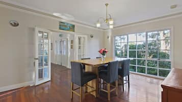 A dining area with a wooden table and four chairs, a chandelier, and a view through large windows.