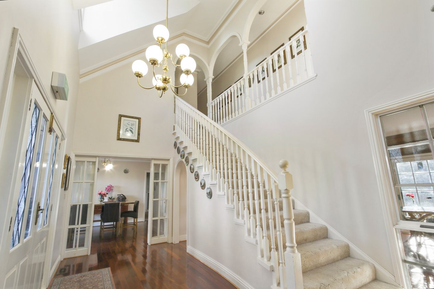 Una imponente escalera con balaustradas blancas y un candelabro, que conduce a un nivel superior.