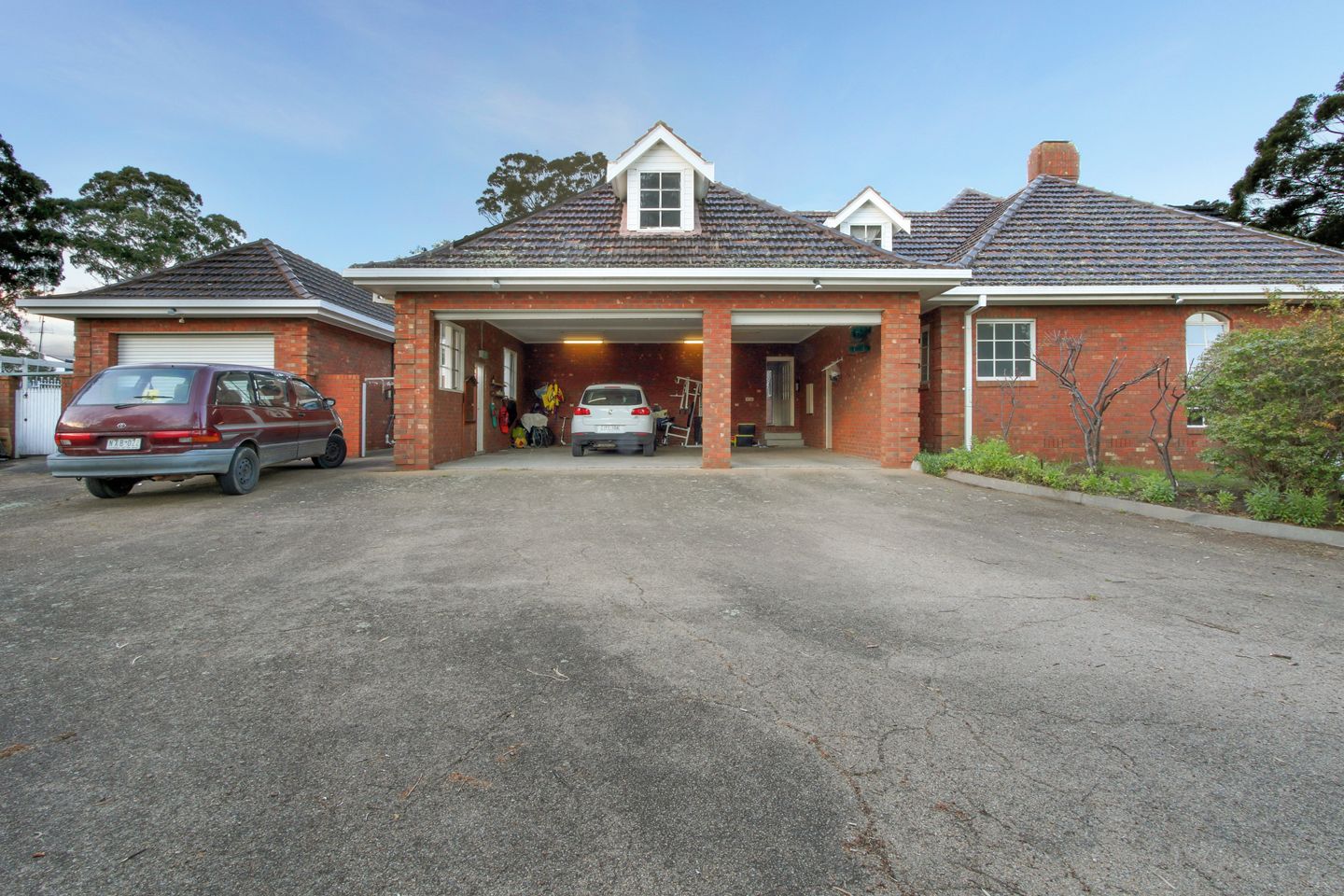 Una casa de ladrillo de dos pisos con garaje, entrada para coches y un pequeño jardín.