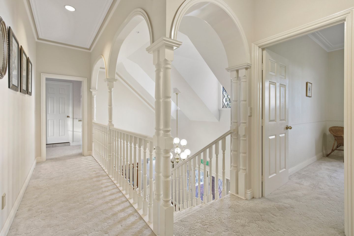 Un pasillo con columnas blancas, una escalera y una puerta que da a otra habitación.