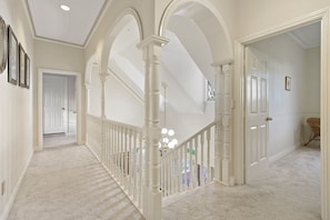 A hallway with white columns, a staircase, and a door leading to another room.