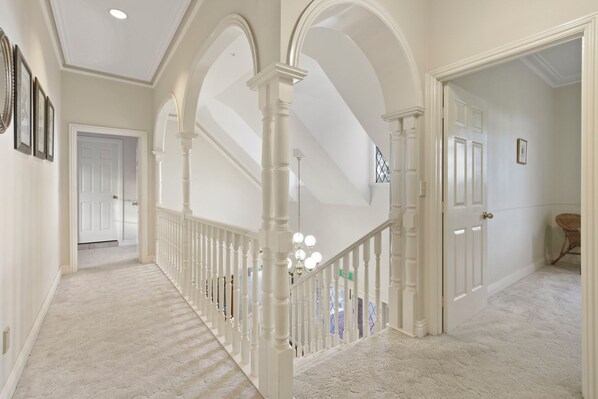 A hallway with white columns, a staircase, and a door leading to another room.