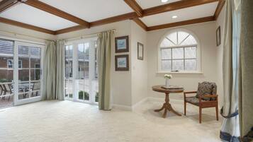 Una habitación amplia con un gran ventanal corredero que da a un área exterior, una mesa redonda de madera con una silla, y una ventana con vistas.