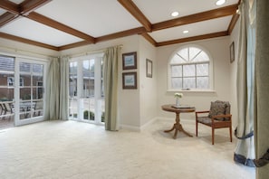 A spacious room with a large sliding glass door leading to an outdoor area, a round wooden table with a chair, and a window with a view.