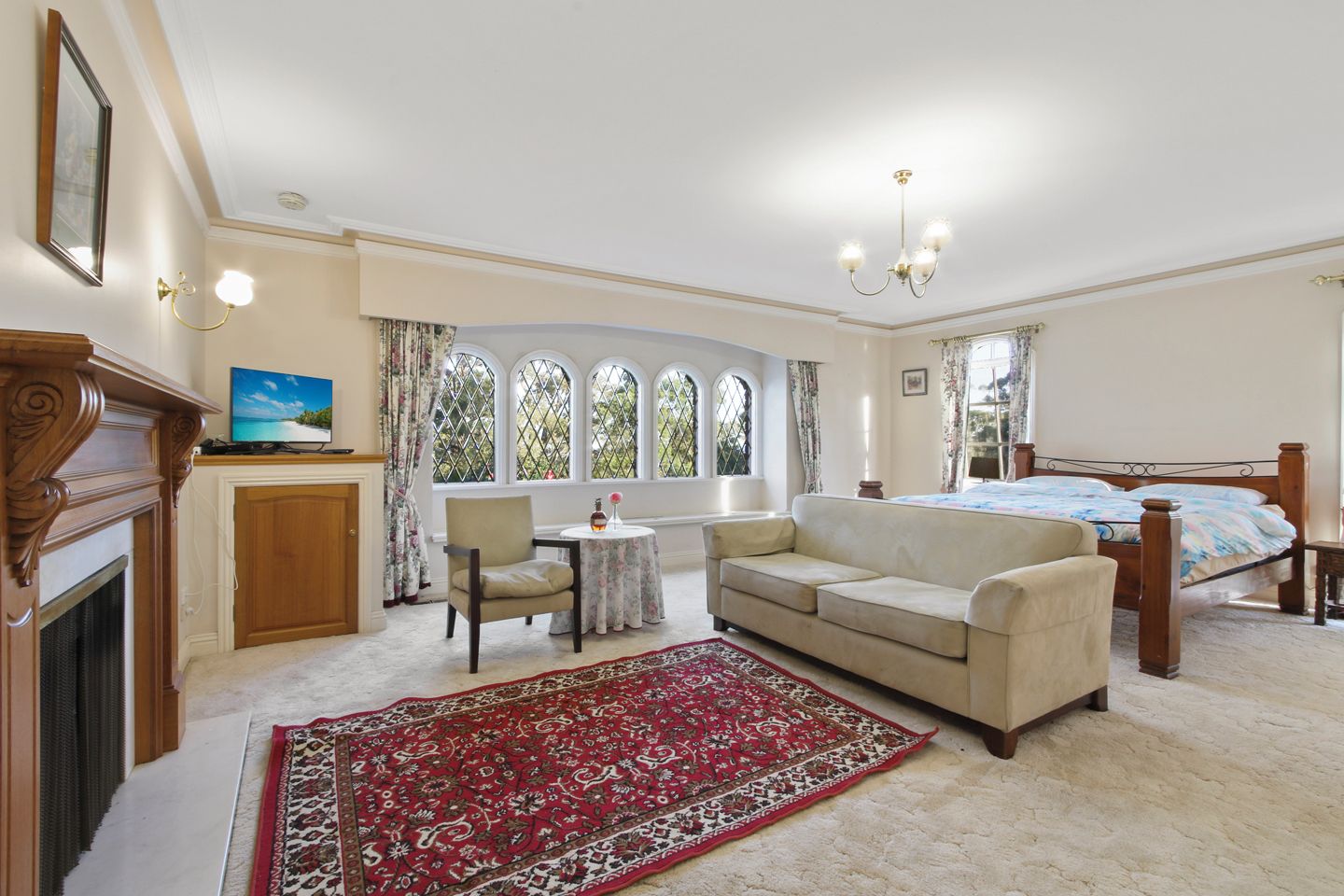 A room with a bed, a sofa, a fireplace, a television, and a large window with curtains.