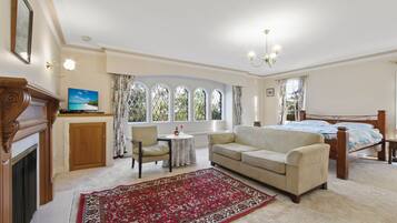 A room with a bed, a sofa, a fireplace, a television, and a large window with curtains.