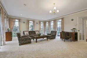 A spacious living room with a high ceiling, large windows, and a chandelier.