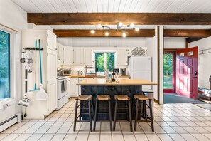 A kitchen with white cabinets, a wooden island with stools, and a red door. - Mashpee Retreat 3BR 2BA Pond Access & Water Views (Mashpee)