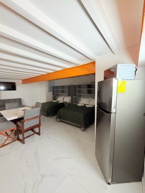 A compact room with a bed, a small table, a chair, a refrigerator, and a television mounted on the wall. - Cathedral Centro Histórico D13 (Guadalajara)