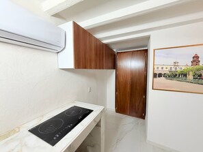 A compact kitchen with a built-in stove, a wooden cabinet, and a wall-mounted air conditioner. - Cathedral Centro Histórico D13 (Guadalajara)