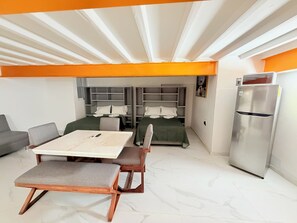 A modern hotel room with a dining table, two beds, a sofa, and a refrigerator. - Cathedral Centro Histórico D13 (Guadalajara)
