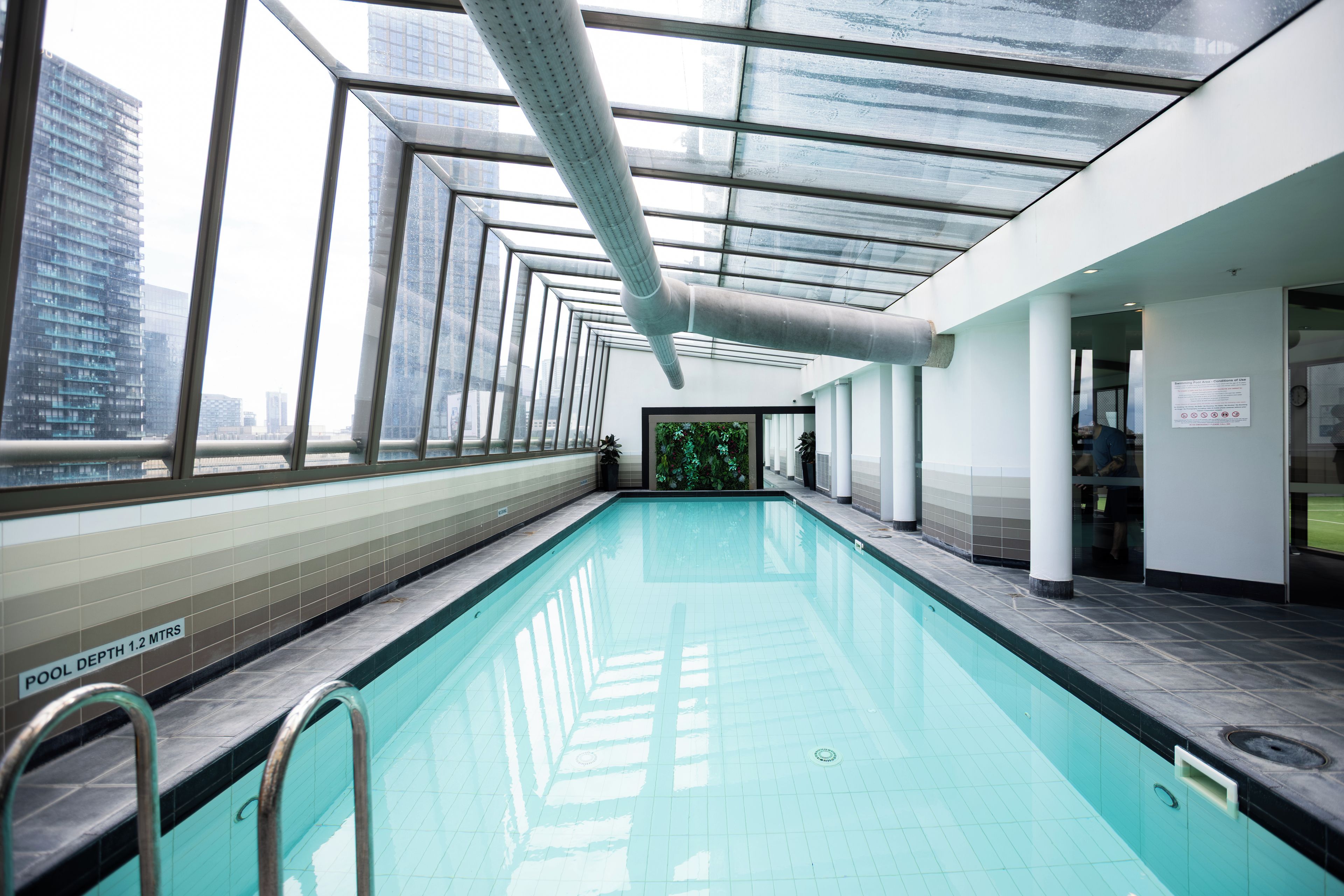 An indoor swimming pool with clear glass walls, a tiled floor, and a sign indicating a pool depth of 1.2 meters.