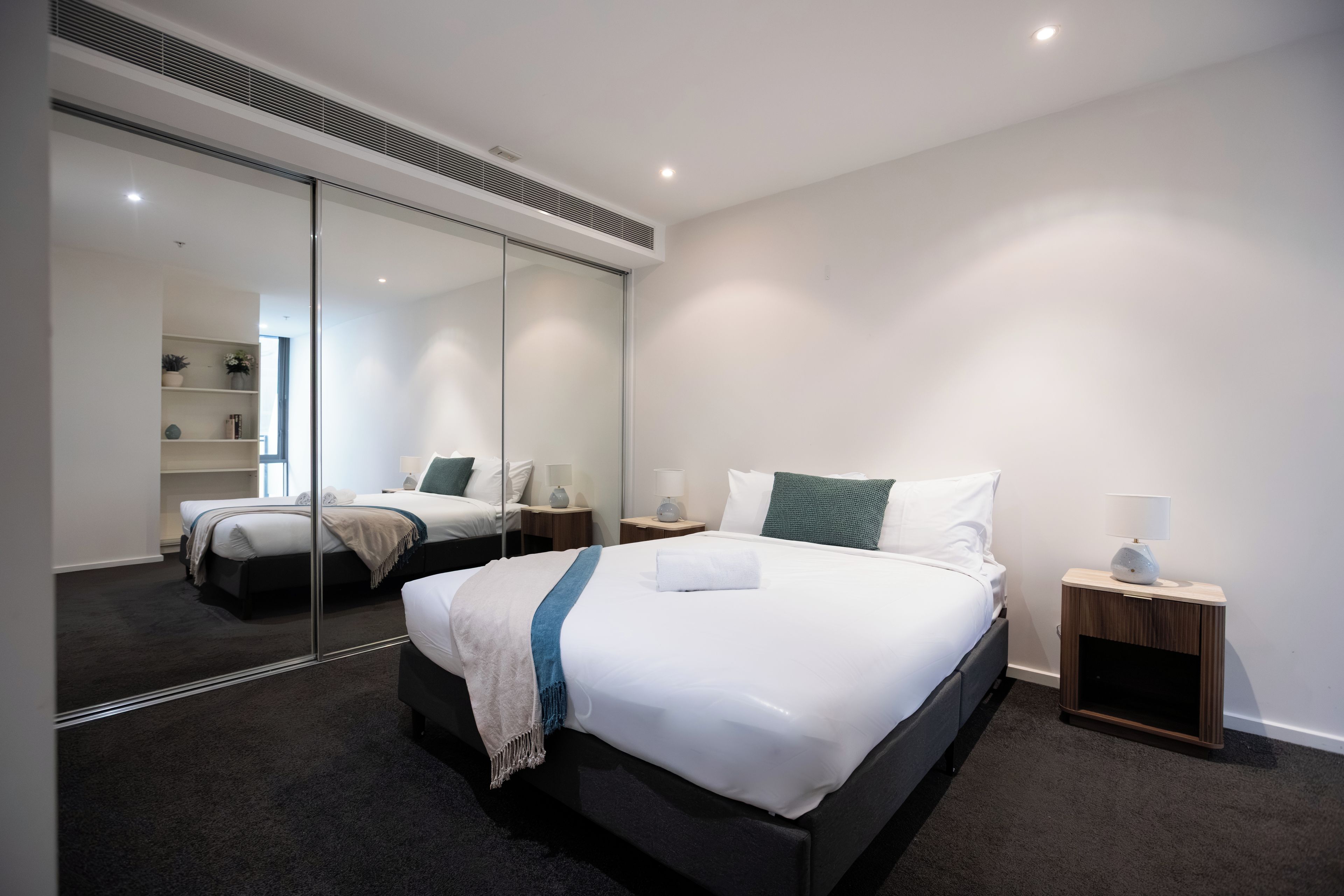 A modern hotel room with a large bed, bedside tables, a mirror, and a view of the adjacent room.