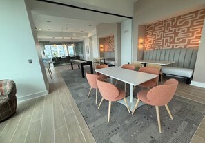 A modern dining area with a long table and pink chairs, a seating area with a patterned wall, and a view of the city through large windows.