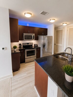 A modern kitchen with stainless steel appliances, wooden cabinets, and a granite countertop.