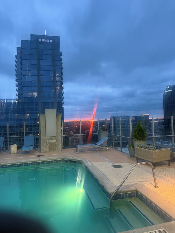 A rooftop pool area with lounge chairs and a view of the city skyline.