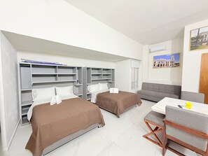 Quarto de hotel com duas camas, um sofá, uma mesa de jantar e uma televisão.