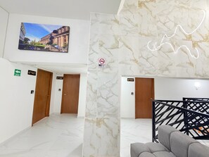 Eine Hotelhalle mit Marmorböden, Holztüren, einem an der Wand montierten Fernseher und einem Rauchverbot-Schild.