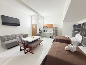 Quarto de hotel compacto com sofá, mesa de jantar, cozinha compacta e cama.