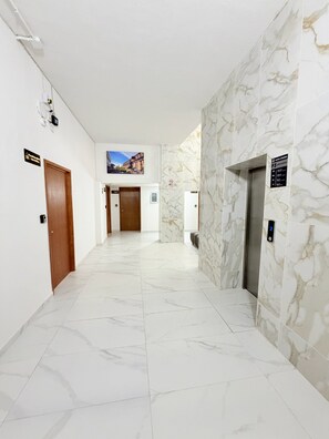 A hotel corridor with marble flooring, a wooden door, a wall-mounted sign, and an elevator. - Cathedral Centro Histórico D14 (Guadalajara)