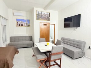 A modern living room with a sofa, a dining table, and a TV mounted on the wall. - Cathedral Centro Histórico D14 (Guadalajara)