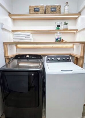 A laundry area with two washing machines, shelves above containing folded towels and a small potted plant. - 3B/2Ba House 5 minutes from The Domain (Austin)