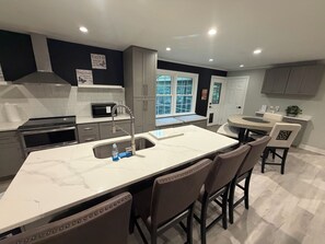 A modern kitchen with a marble island, stainless steel appliances, and a view to the outdoors.