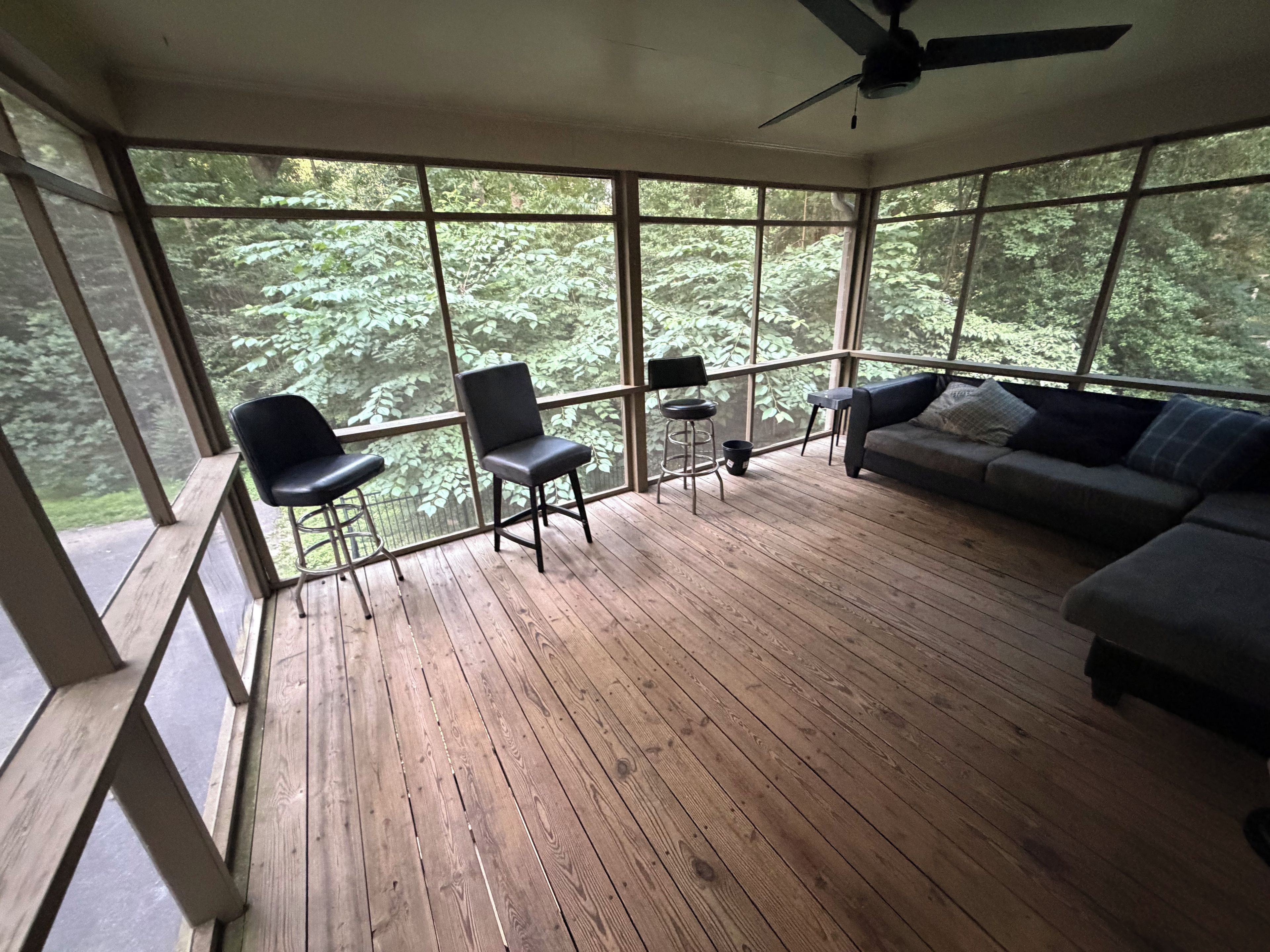 Une pièce avec un plancher en bois, un ventilateur de plafond, un canapé, deux fauteuils et une petite table.