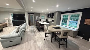 Una sala de estar moderna con un sofá, un comedor con una mesa redonda y una cocina con electrodomésticos integrados.