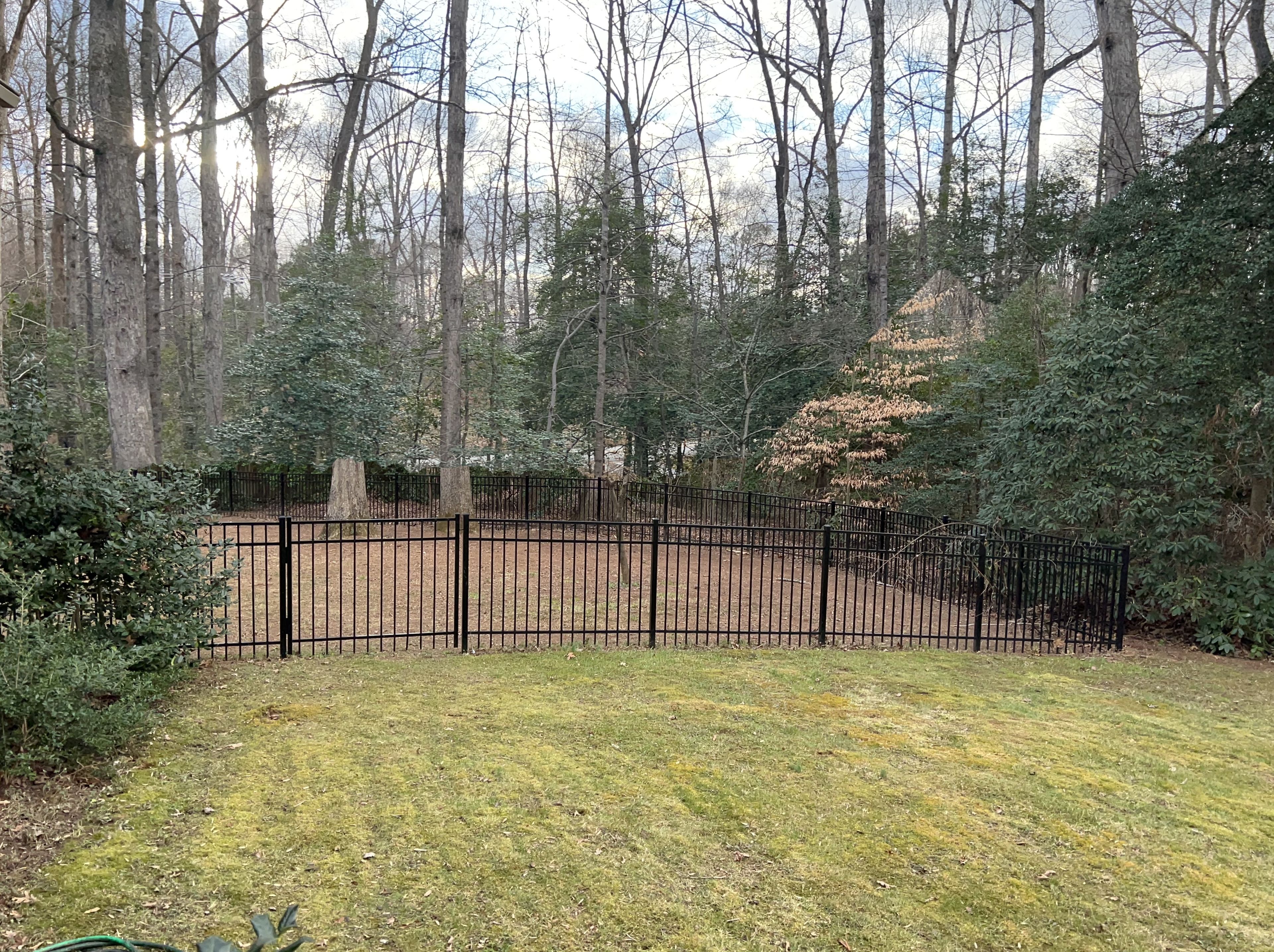 A fenced yard with a grassy area, trees, and a hill in the background.