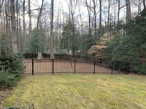 A fenced yard with a grassy area, trees, and a hill in the background.
