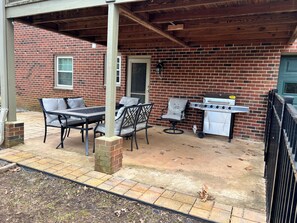 Un patio al aire libre con pared de ladrillo, una mesa con sillas y una estufa de gas portátil.
