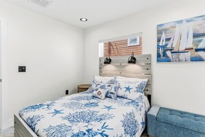 A bedroom with a bed, a headboard with a window, a nightstand, and a painting on the wall. - Aqua Tides Cottage #4 at White Sands  -1br/1bath-steps to beach (Indian Rocks Beach)