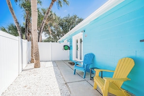 A patio area with a white fence, a blue wall, and two Adirondack chairs. - Aqua Tides Cottage #4 at White Sands  -1br/1bath-steps to beach (Indian Rocks Beach)