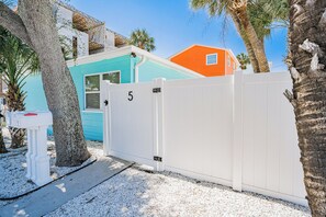 A gated area with a mailbox, a palm tree, and a building with a blue and orange facade. - Aqua Tides Cottage #5|1br/1ba steps to beach (Indian Rocks Beach)